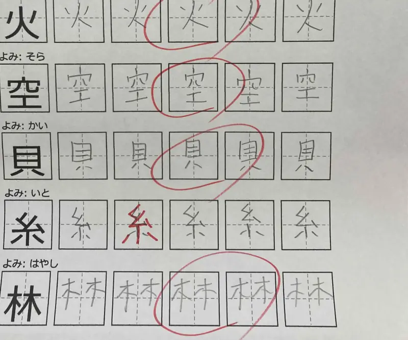 漢字練習プリント。鉛筆で書いた漢字と赤ペンの丸付けが並んでいる